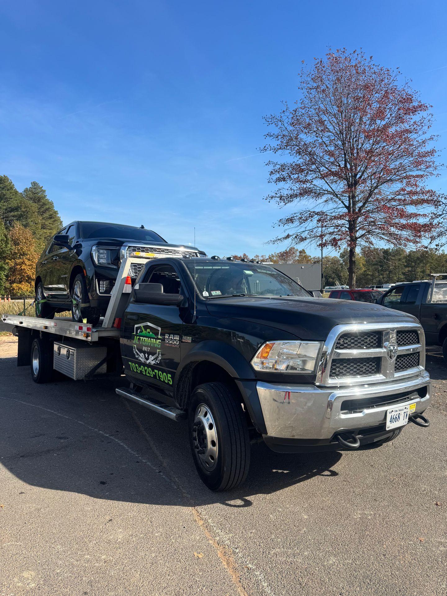 Tow truck carrying a black SUV under a clear blue sky, with autumn trees in the background.