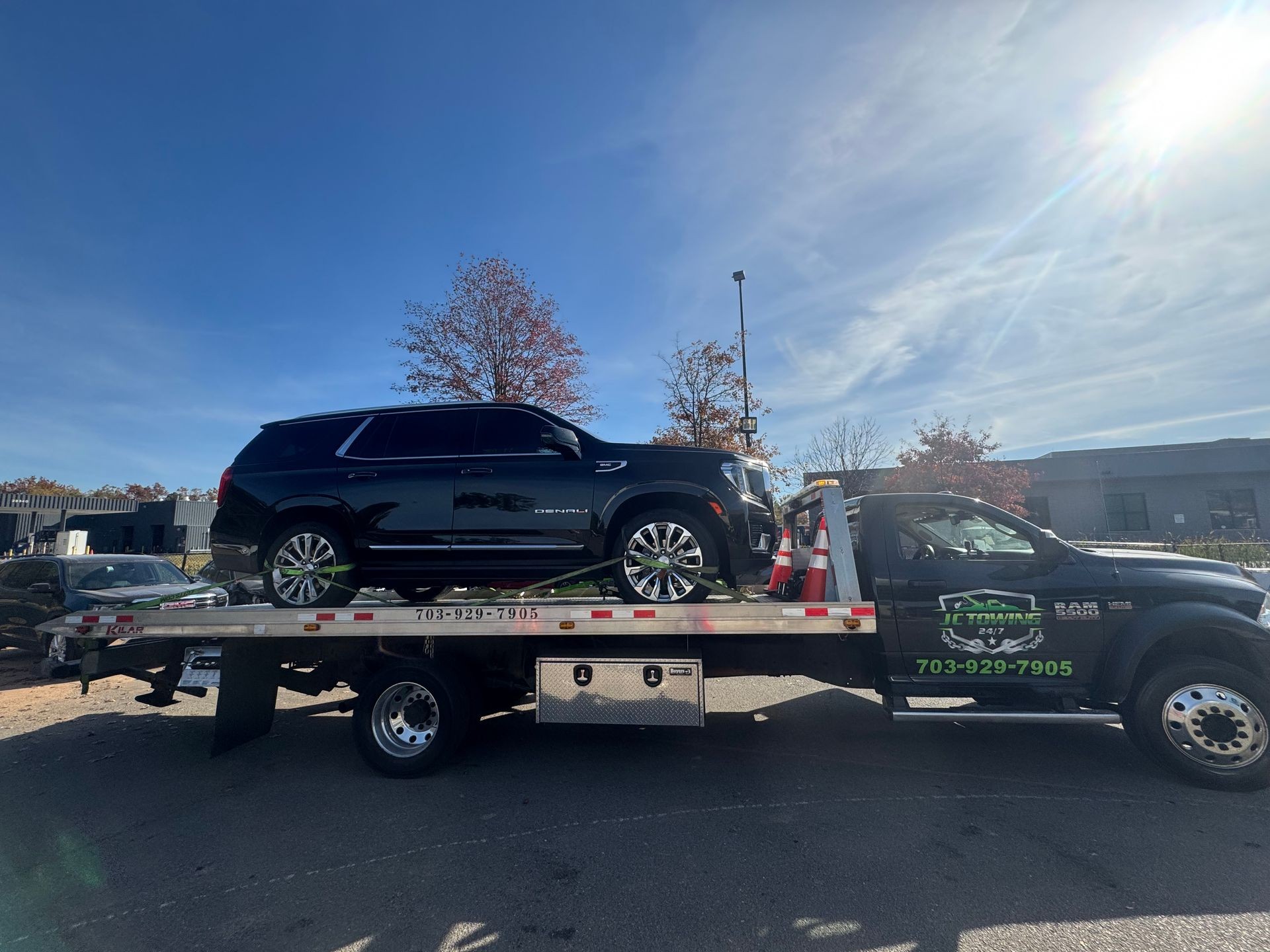 Black SUV on a flatbed tow truck in a parking lot under a clear sky.