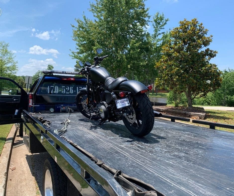 Motorcycle secured on a flatbed tow truck under a clear blue sky.