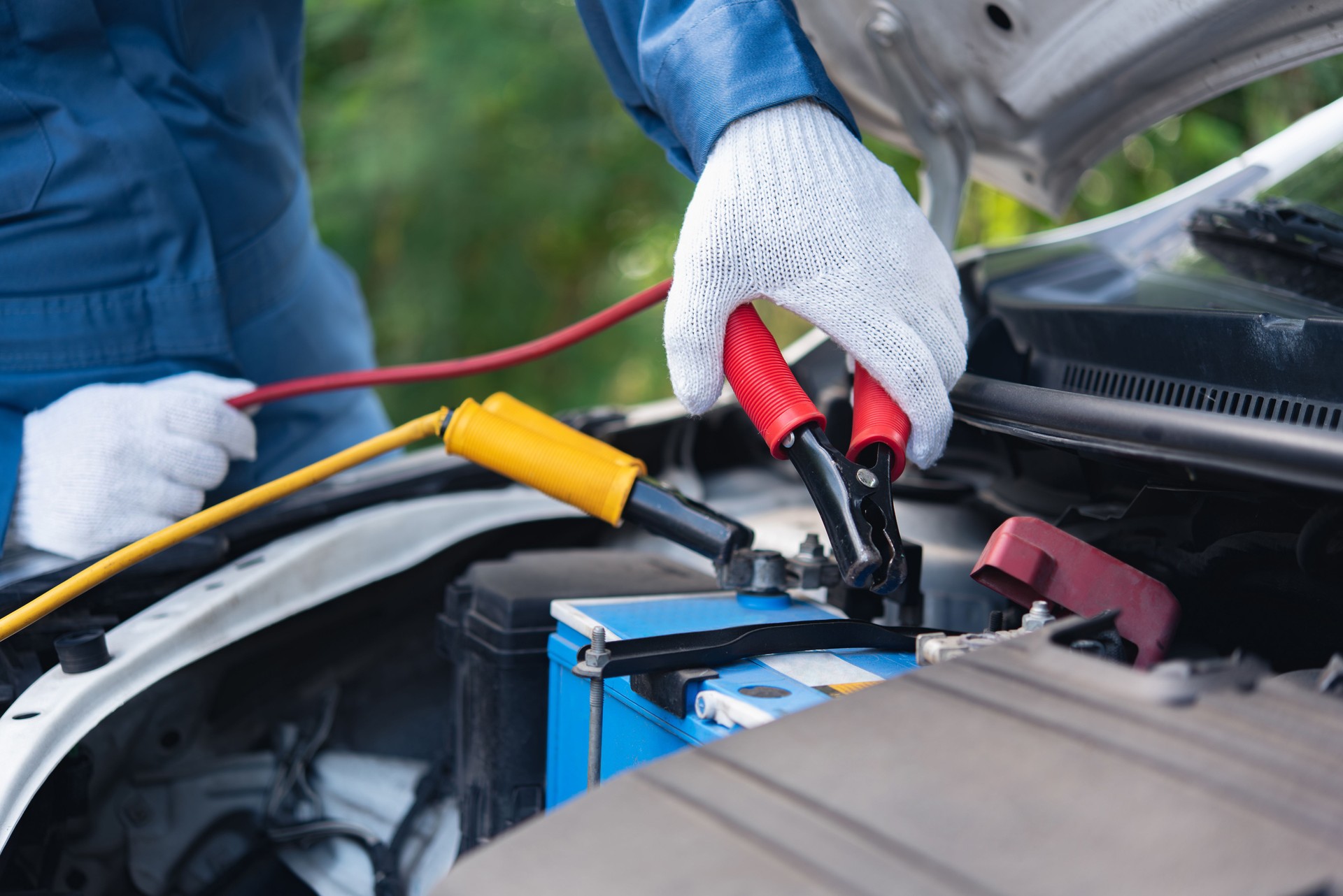 a mechanic using jumper cables to manually power a car's battery