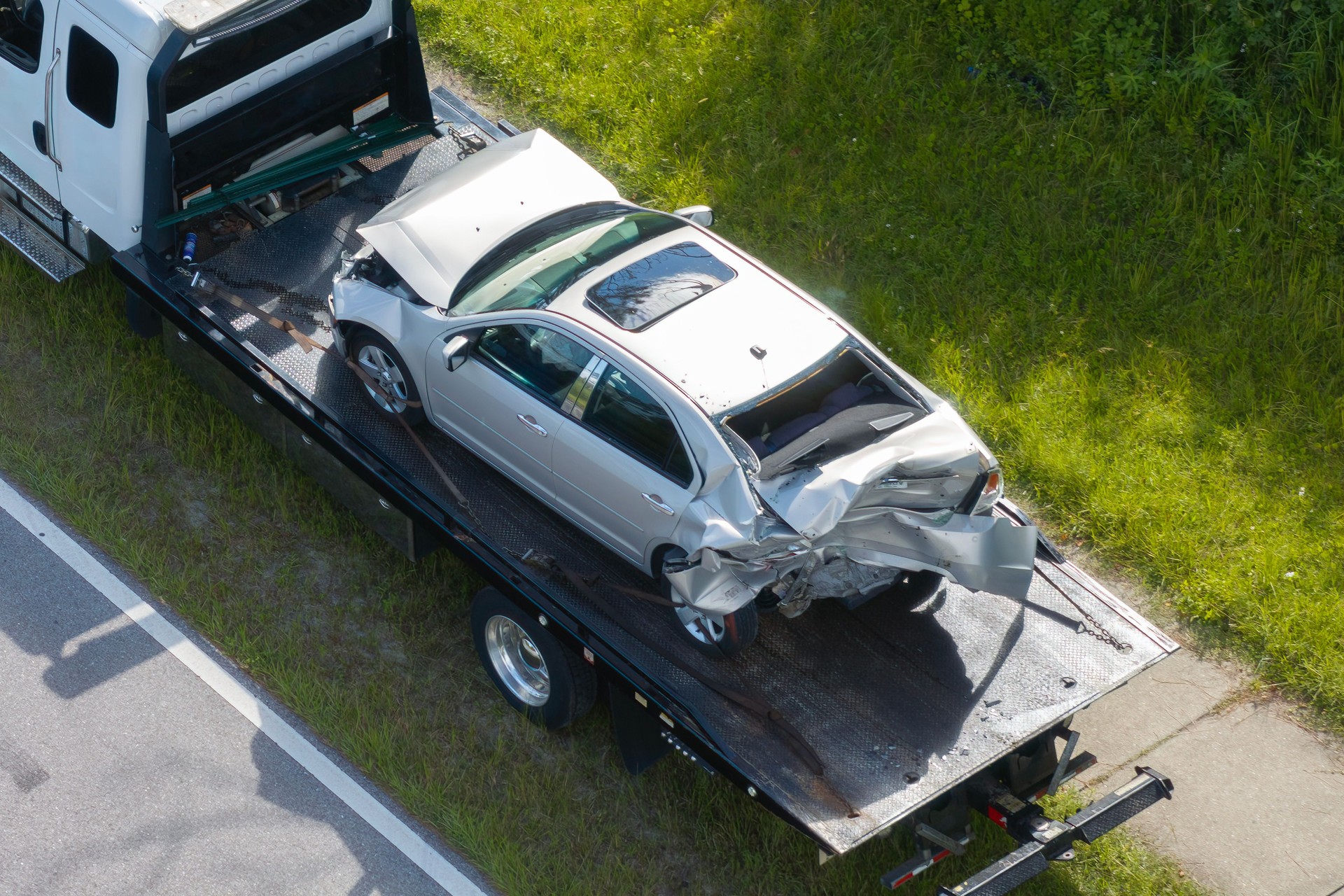 Tow truck hauling smashed vehicle on car accident site. Emergency services personnel responding to traffic crash on American street. First responders helping on road in the USA